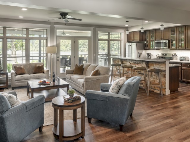 A cozy, well-lit living room with comfortable sofas, a kitchen island, and large windows overlooking nature.
