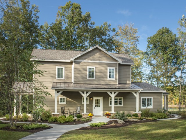 A charming two-story house with a front porch, surrounded by green trees, a well-maintained lawn, and decorative plants.