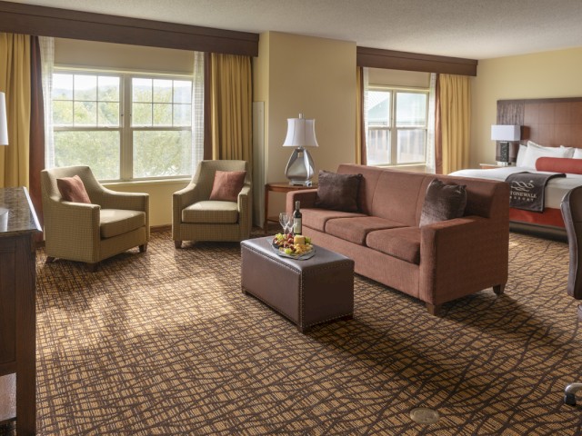 This is a hotel room with a sitting area, large windows, a bed, and various furniture including lamps and cushions.