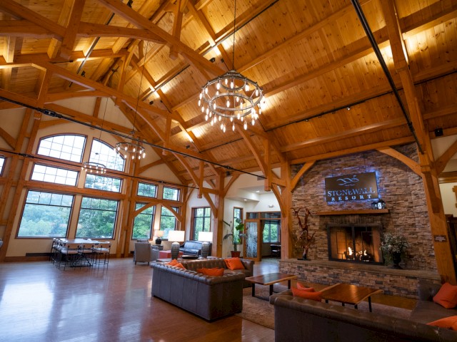A spacious, cozy lodge lounge with a large stone fireplace, wooden beams, a chandelier, and seating area at Stonewall Resort.