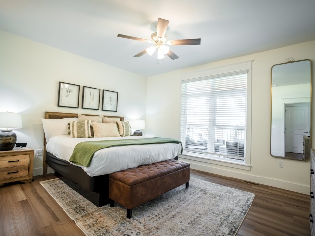 Cozy bedroom with a queen bed, wooden furniture, a bench, large mirror, and natural light from a big window.