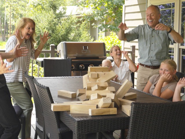 A family enjoys a lively game of giant Jenga on their outdoor patio on a sunny day.