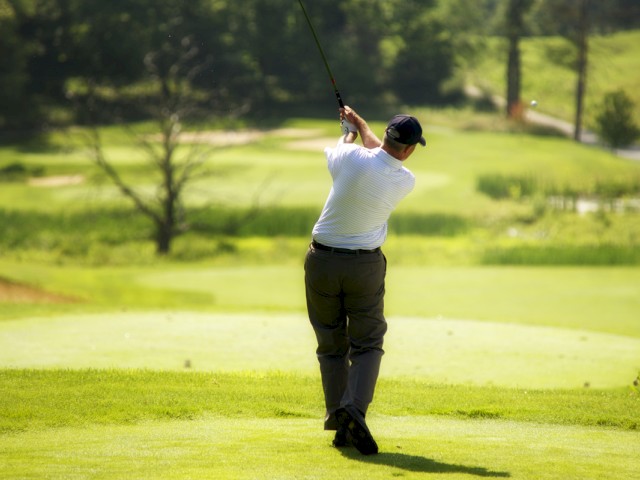 A person is swinging a golf club on a golf course with a lush, green landscape in the background and a tree in the distance, ending the sentence.