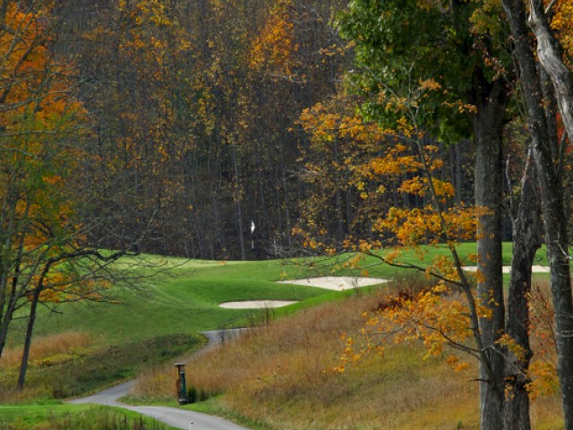 The image depicts a fall scene at a golf course with autumn trees, a golf cart path, golfers playing, and a golf cart near the green surrounded by fall foliage.