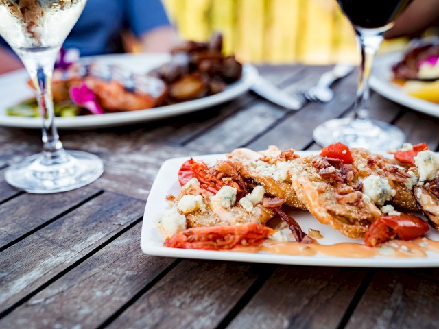 A plate of food with what appears to be roasted tomatoes, cheese, and garnish on a wooden table, accompanied by glasses of wine and other dishes.