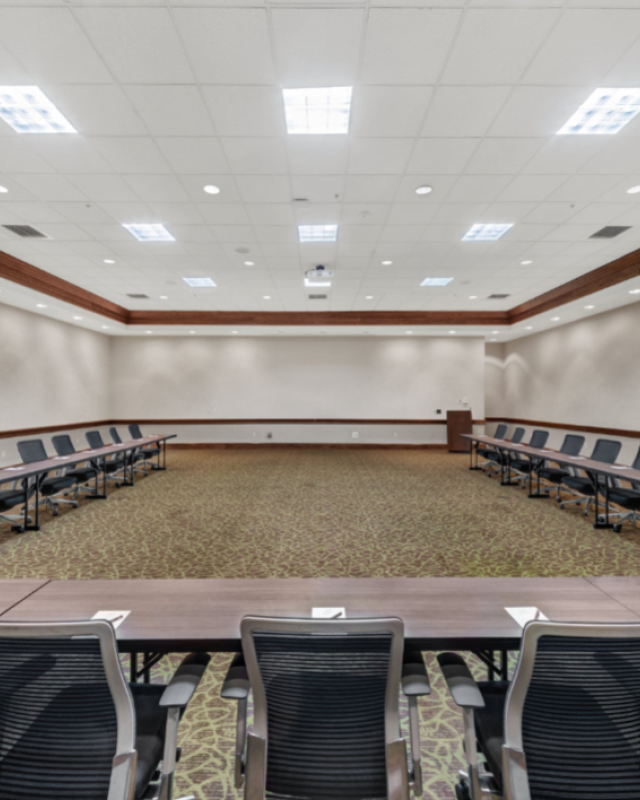 This image shows an empty, well-lit conference room with a U-shaped arrangement of tables and chairs, suitable for meetings or presentations.