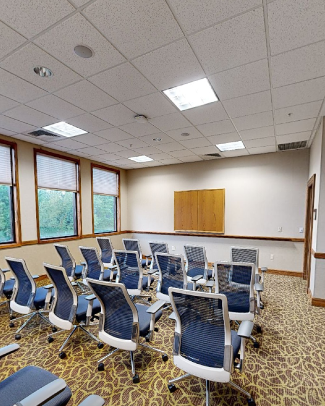 A conference or meeting room with multiple chairs, windows, and a cabinet, ready for a presentation or discussion.