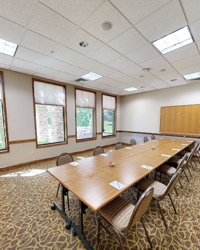 A conference room with a large table, chairs, four windows, and a corkboard on the wall.