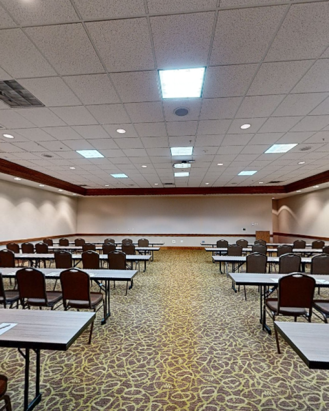 This is an empty conference room with tables and chairs, set up for a meeting or event, with a clock on the wall and ceiling lights.
