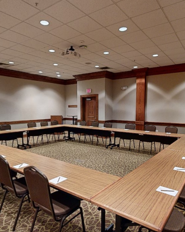 This image shows a large, empty conference room arranged in a U-shape with chairs and notepads, and appears ready for a meeting or presentation.