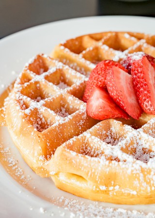 A plate of waffles topped with powdered sugar and fresh strawberry slices.