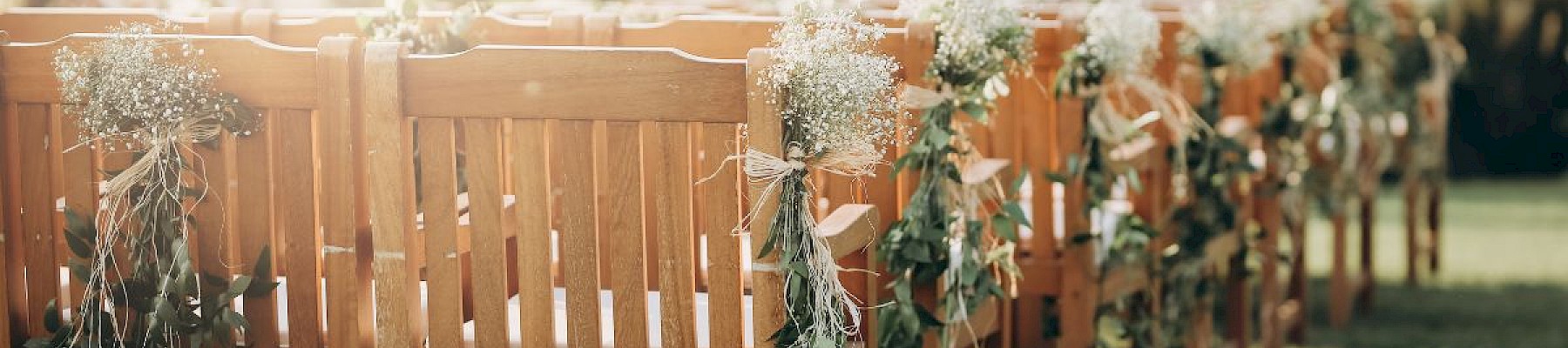 Wooden chairs decorated with flowers and greenery are set up outdoors, likely for a wedding or special event.