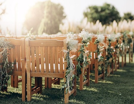 Wooden chairs decorated with flowers and greenery are set up outdoors, likely for a wedding or special event.