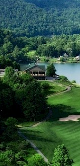 A scenic golf course with green fairways and sand traps, surrounded by trees, lakes, and a lush, forested backdrop.