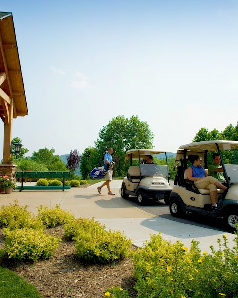 People arriving at a golf course, boarding golf carts near a clubhouse on a sunny day.