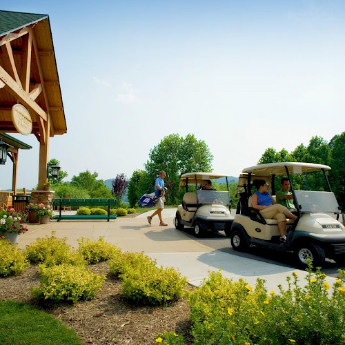 People arriving at a golf course, boarding golf carts near a clubhouse on a sunny day.