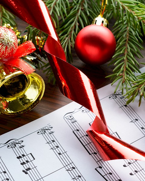 Christmas decorations with ornaments, a tree branch, a bell, ribbon, and sheet music for holiday celebrations.