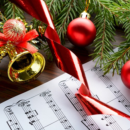 Christmas decorations with ornaments, a tree branch, a bell, ribbon, and sheet music for holiday celebrations.