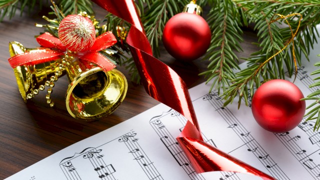Christmas decorations with ornaments, a tree branch, a bell, ribbon, and sheet music for holiday celebrations.
