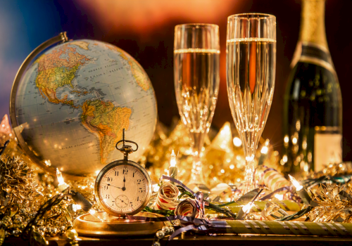 A globe, a stopwatch, two champagne glasses, a bottle of champagne, and holiday decorations with lights.