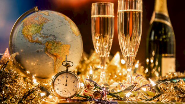 A globe, a stopwatch, two champagne glasses, a bottle of champagne, and holiday decorations with lights.