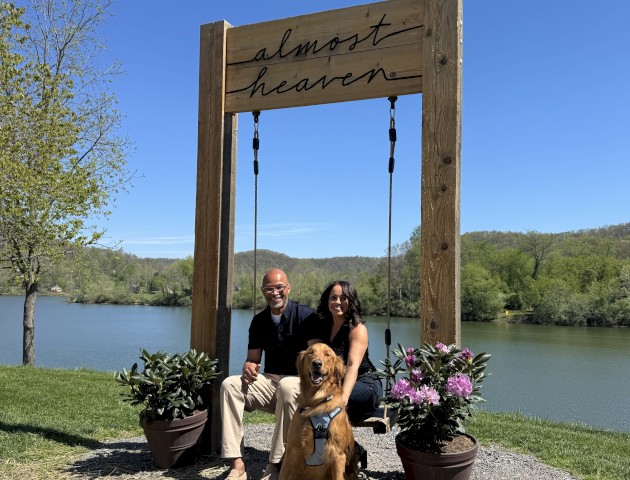 A couple and their dog sit on a swing near a lake, with a 
