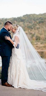 A bride and groom share an intimate moment outdoors with a scenic lake and mountains in the background, celebrating their wedding day.