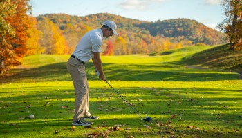 A man in golf attire prepares to tee off on a scenic golf course during autumn.