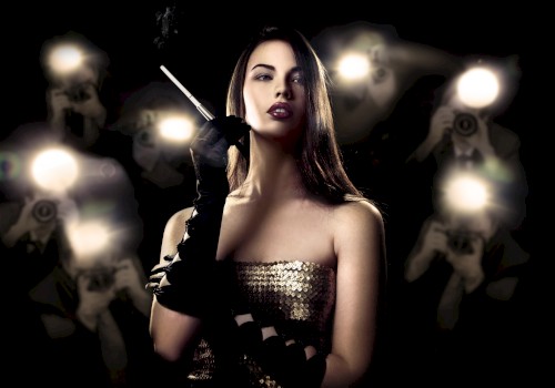 A woman with dark hair, wearing a strapless sequined dress and black gloves, holds a cigarette in front of flashing photographers.