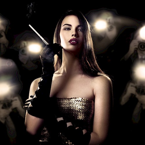 A woman with dark hair, wearing a strapless sequined dress and black gloves, holds a cigarette in front of flashing photographers.
