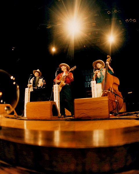 A band performs on stage with old-fashioned instruments, under bright lights, with light bulbs on ground.