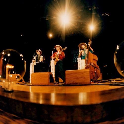 A band performs on stage with old-fashioned instruments, under bright lights, with light bulbs on ground.