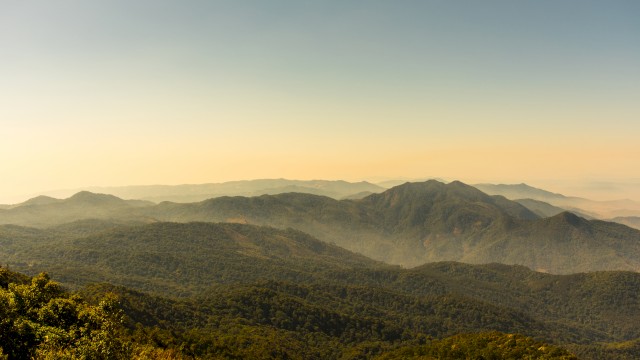 A scenic view of mountain ranges under a clear sky during dusk, showcasing lush greenery and distant rolling hills in a tranquil landscape.