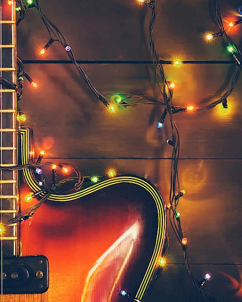 An electric guitar with colorful string lights wrapped around it, illuminated on a dark wooden surface.