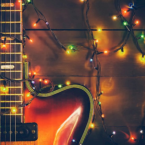 An electric guitar with colorful string lights wrapped around it, illuminated on a dark wooden surface.