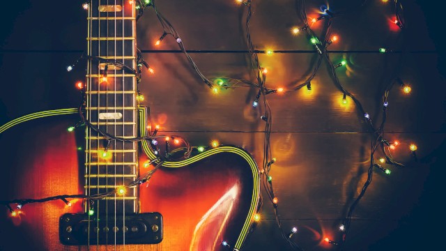 An electric guitar with colorful string lights wrapped around it, illuminated on a dark wooden surface.