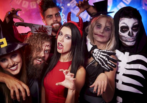A group of people dressed in Halloween costumes, including a witch, devil, skeleton, and others, celebrating at a party.