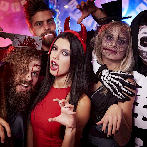 A group of people dressed in Halloween costumes, including a witch, devil, skeleton, and others, celebrating at a party.