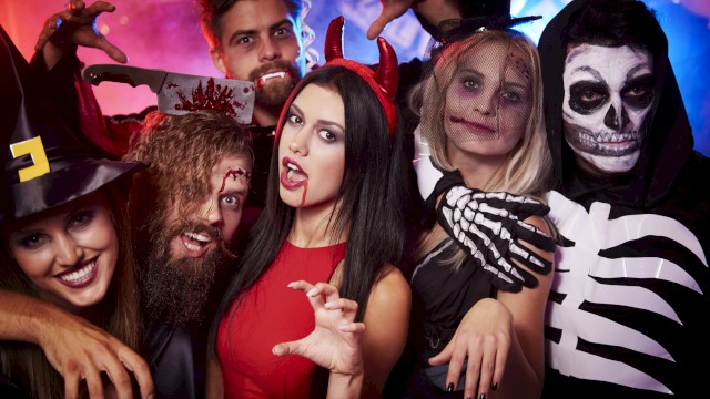 A group of people dressed in Halloween costumes, including a witch, devil, skeleton, and others, celebrating at a party.
