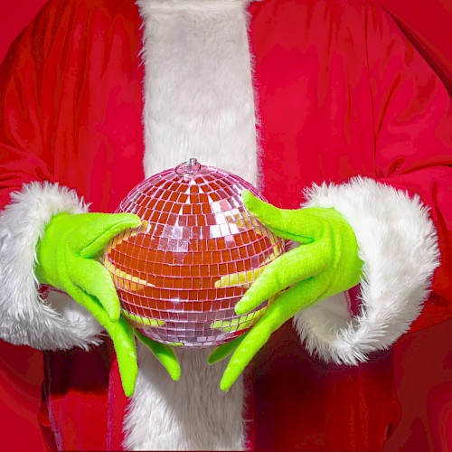 A person dressed as Santa, wearing green gloves, holding a disco ball with a red background.