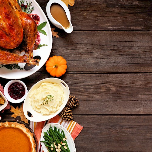 A Thanksgiving feast with roast turkey, mashed potatoes, green beans, cranberry sauce, pumpkin pie, and stuffing on a wooden table.