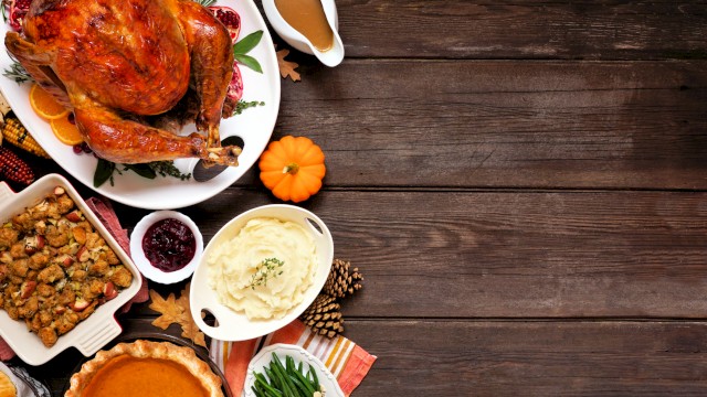 A Thanksgiving feast with roast turkey, mashed potatoes, green beans, cranberry sauce, pumpkin pie, and stuffing on a wooden table.