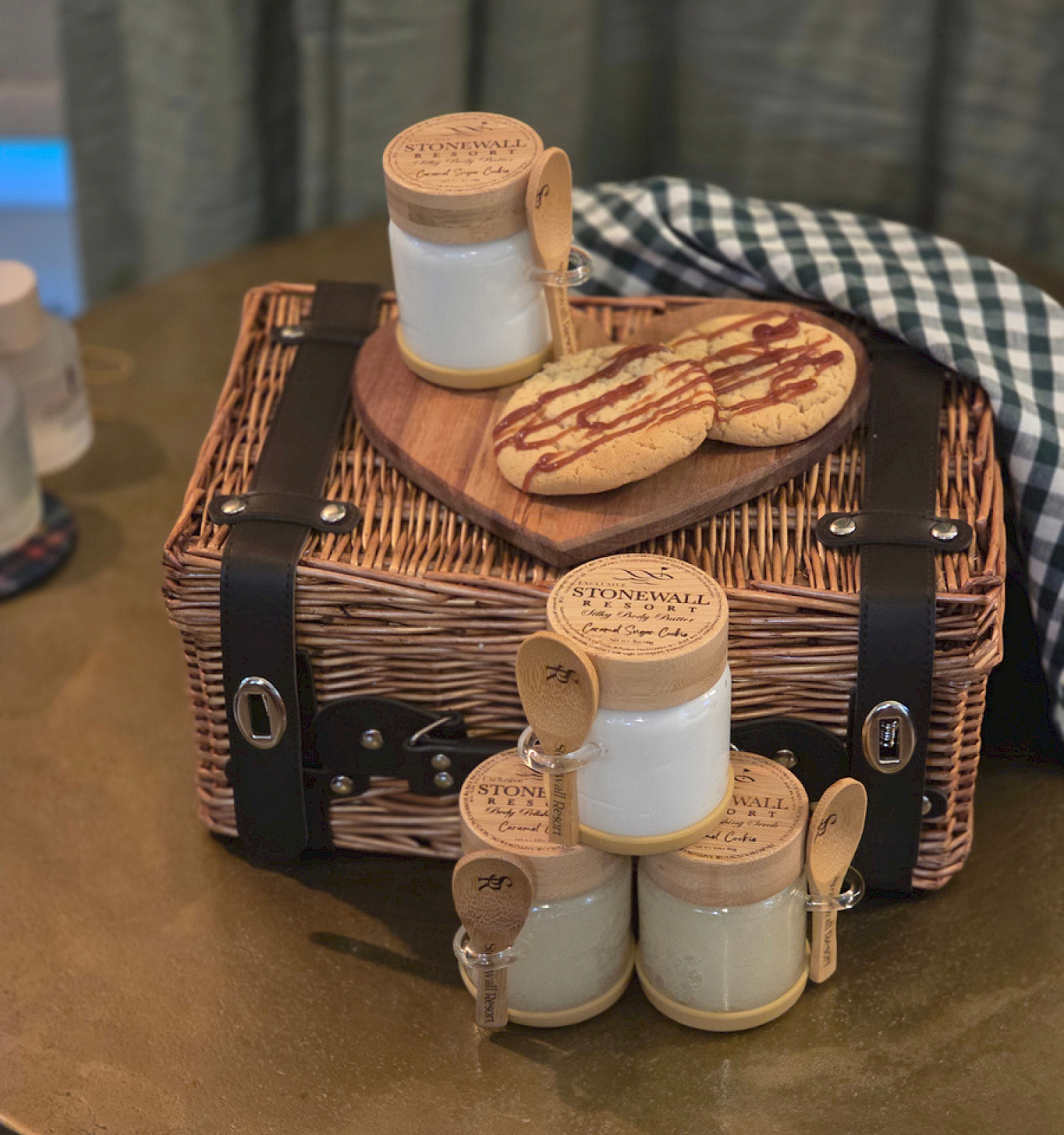 Small jars of sugar, a wooden tray with cookies, a basket, and a checkered cloth on a table.