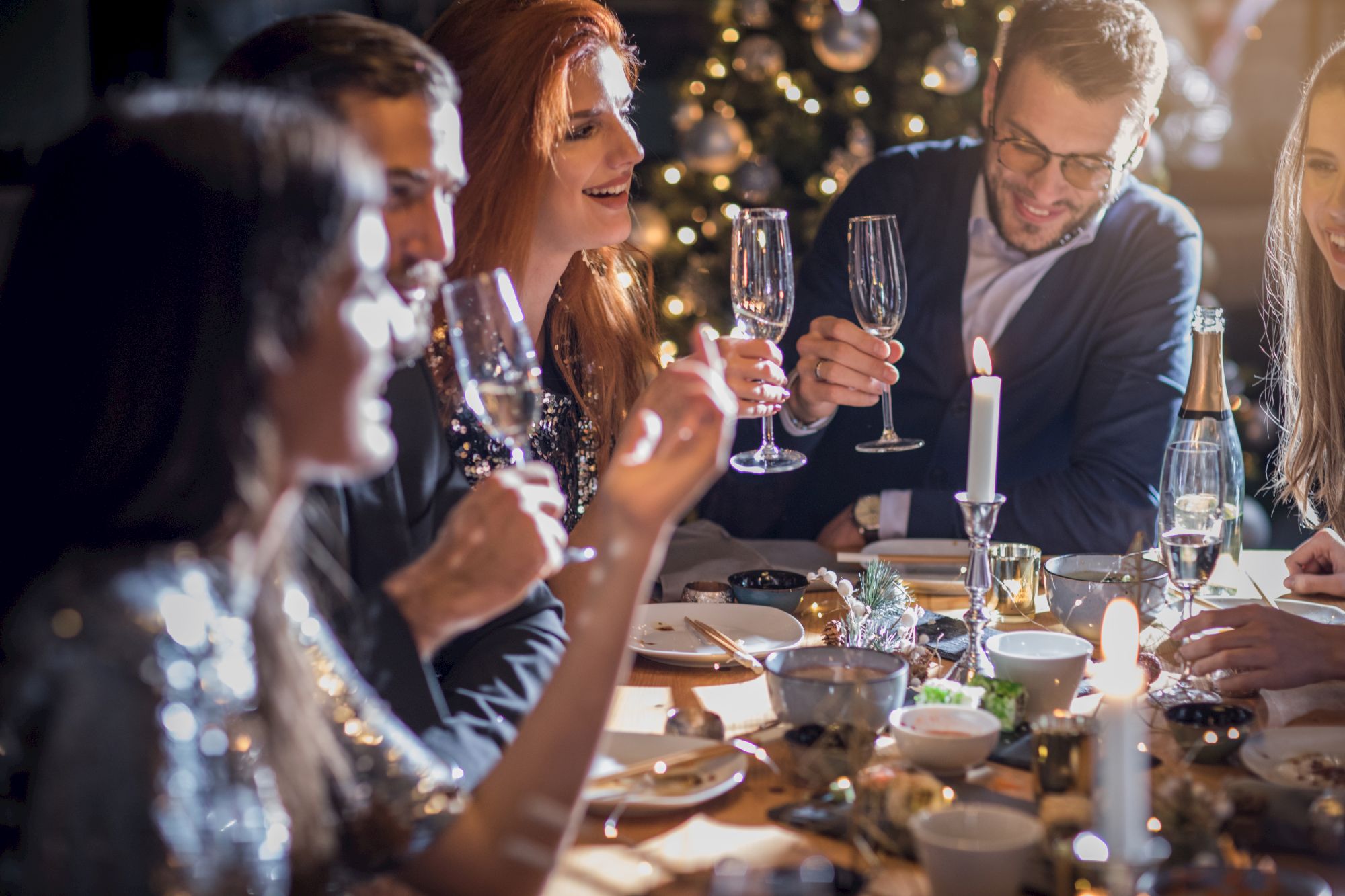 A group of people are gathered around a festive dinner table, toasting with champagne glasses, and enjoying a celebratory meal.