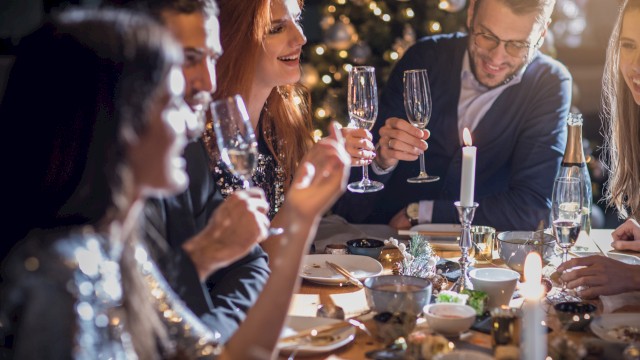 A group of people celebrating at a dinner table, holding champagne glasses, with a Christmas tree in the background.