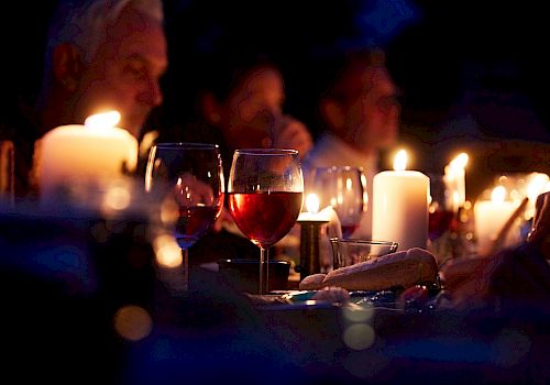 The image shows a dimly lit dinner scene with wine glasses, candles, and people seated at a table.