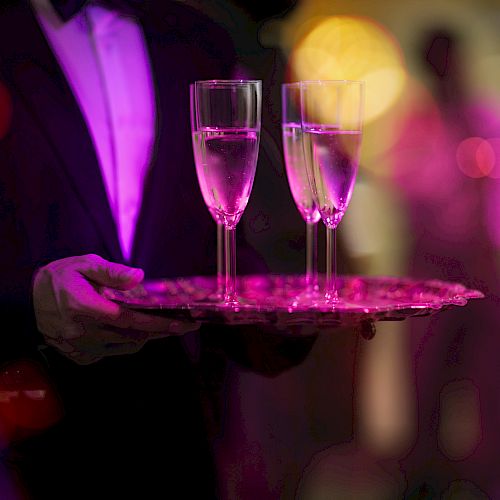 A waiter holding a tray with two champagne flutes in a dimly lit environment.