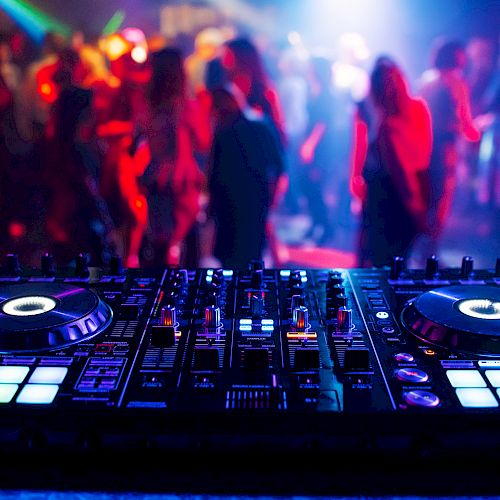 A DJ mixer with illuminated controls is in the foreground, while a crowded dance floor with colorful lights is in the background of a club.