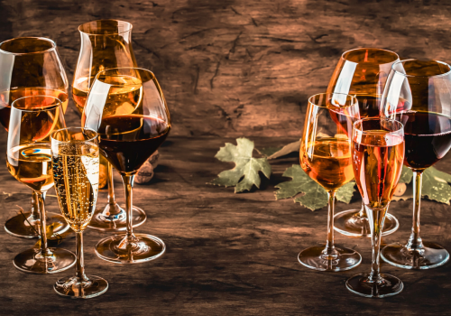 The image shows a variety of wine glasses filled with different types of wine, set on a rustic wooden table with grape leaves as decoration.