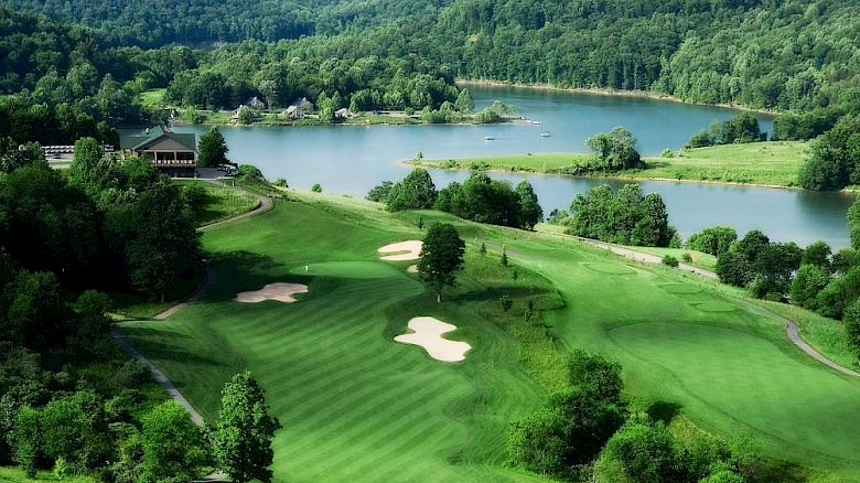 This image shows a scenic view of a golf course with well-manicured greens, sand bunkers, surrounded by a lush forest and a serene lake in the background.